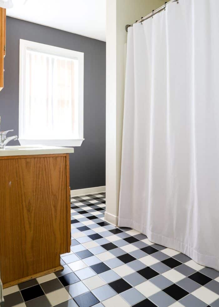 Bathroom with buffalo plaid tiles and solid grey wallpapered accent wall