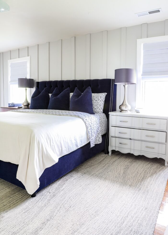 Navy blue bed with blue and white flowered bedding against a grey board and batten accent wall