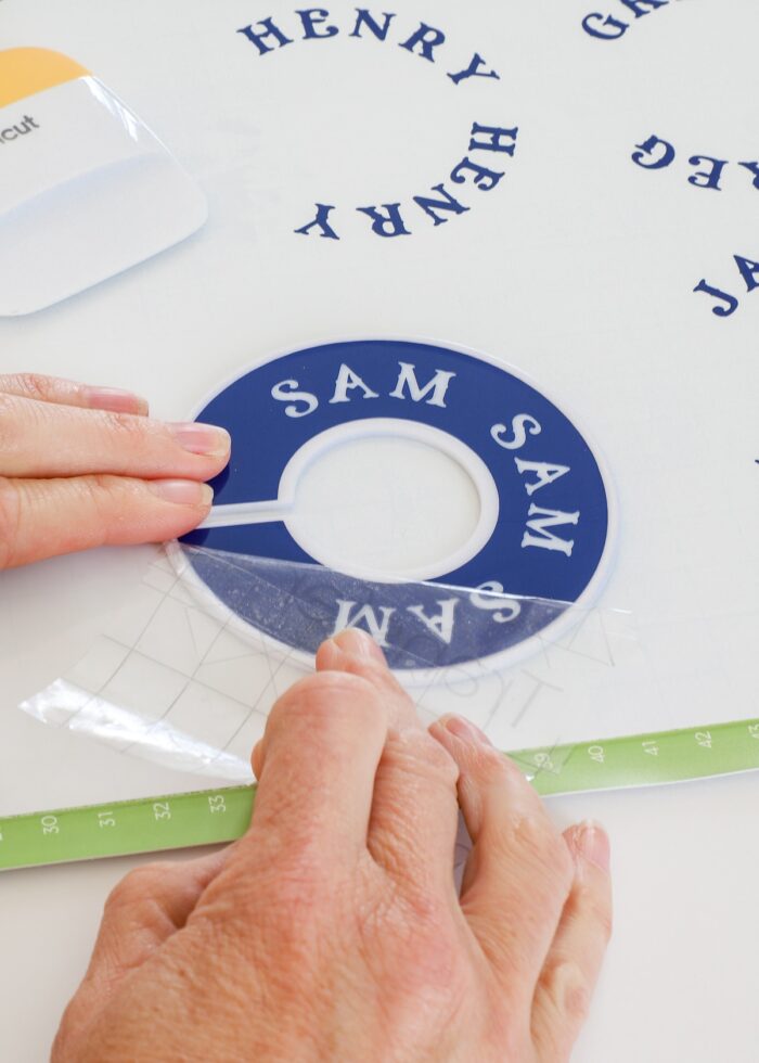 Hand removing transfer tape from blue vinyl label placed onto round closet divider