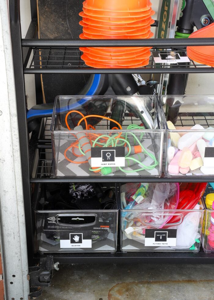 Plastic bins on a sports equipment storage rack holding jump ropes, gloves, chalk, etc.