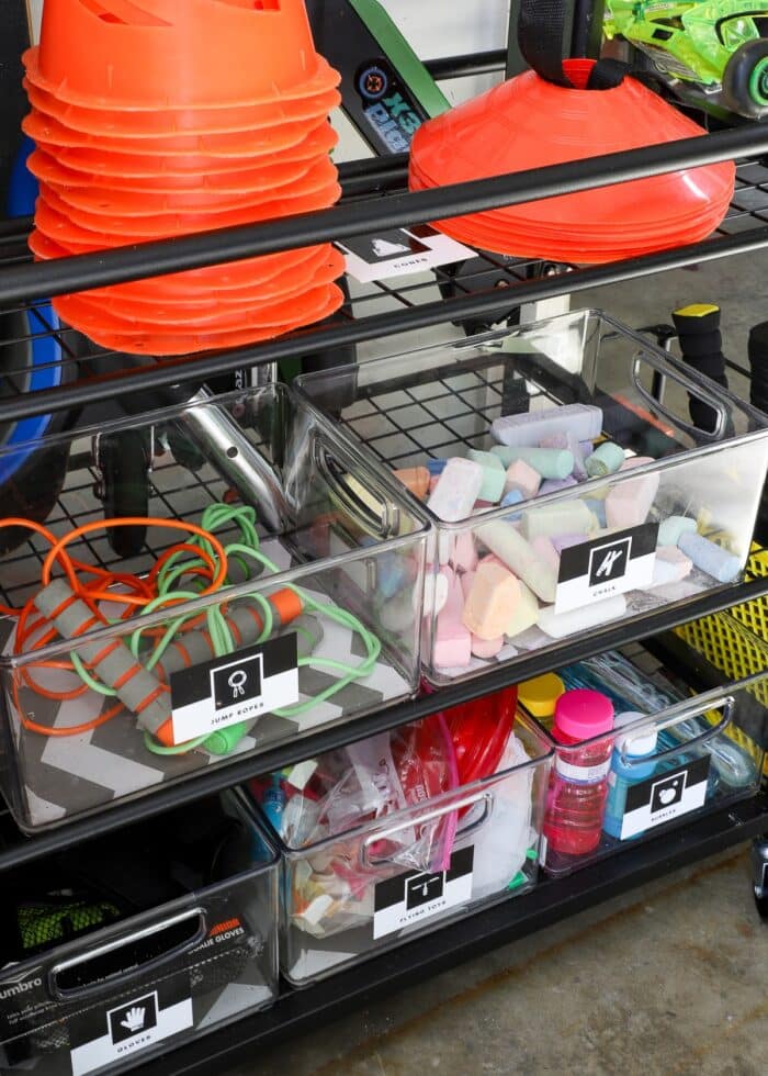Plastic bins on the shelves of a sports equipment storage rack holding outdoor toys