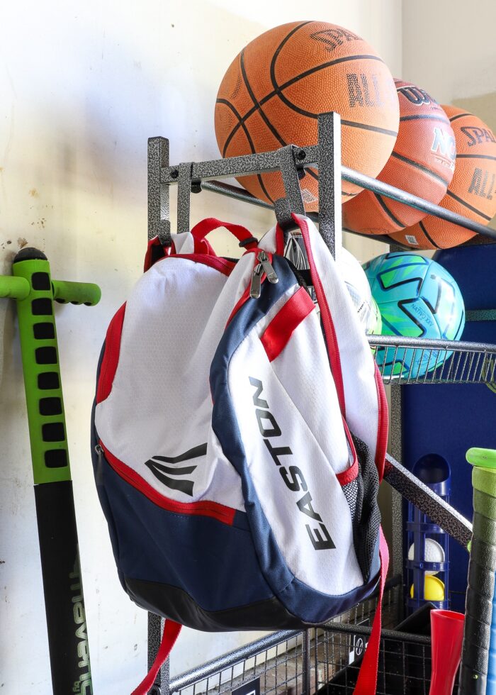 A baseball backpack hanging on two hooks on a sports equipment storage rack