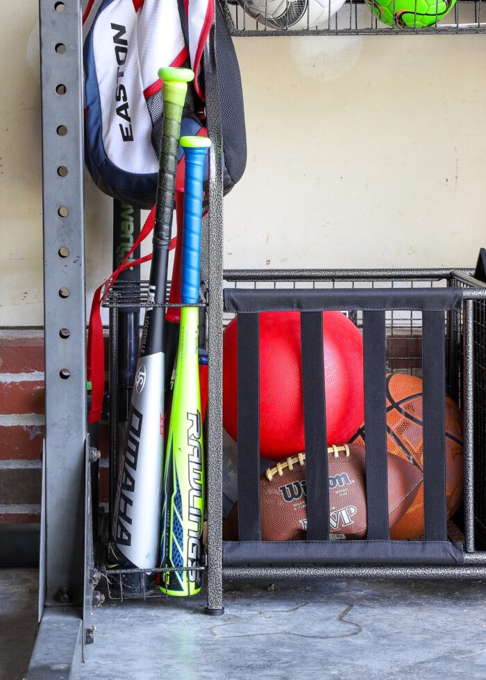 Baseball bats and balls inside a sports equipment storage rack along a garage wall