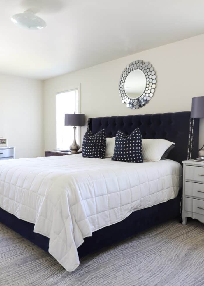 Beige rental master bedroom with navy blue bed and grey lamps