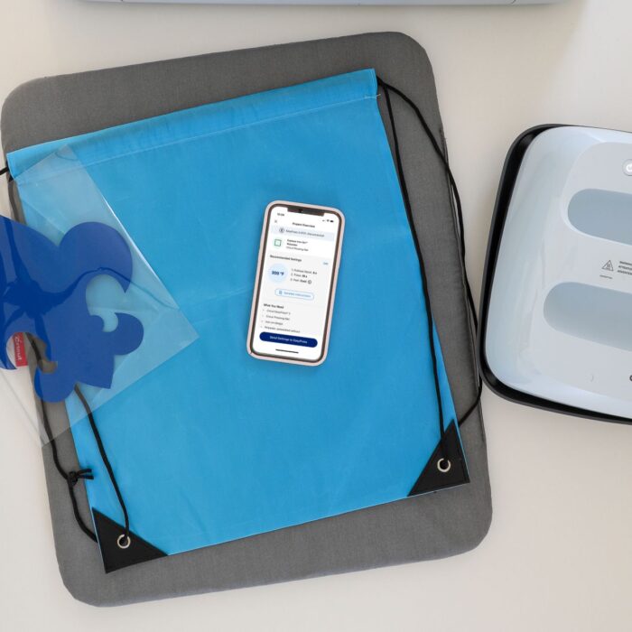 Blue drawstring backpack shown with Cricut EasyPress 3 and Cricut Heat App on iPhone