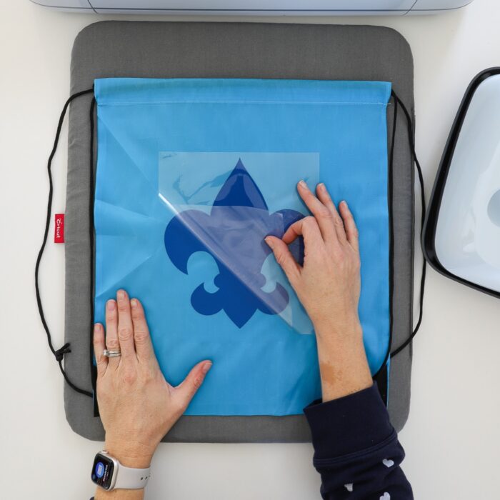 Hands peeling away clear carrier sheet off Cub Scout decal on a light blue drawstring backpack