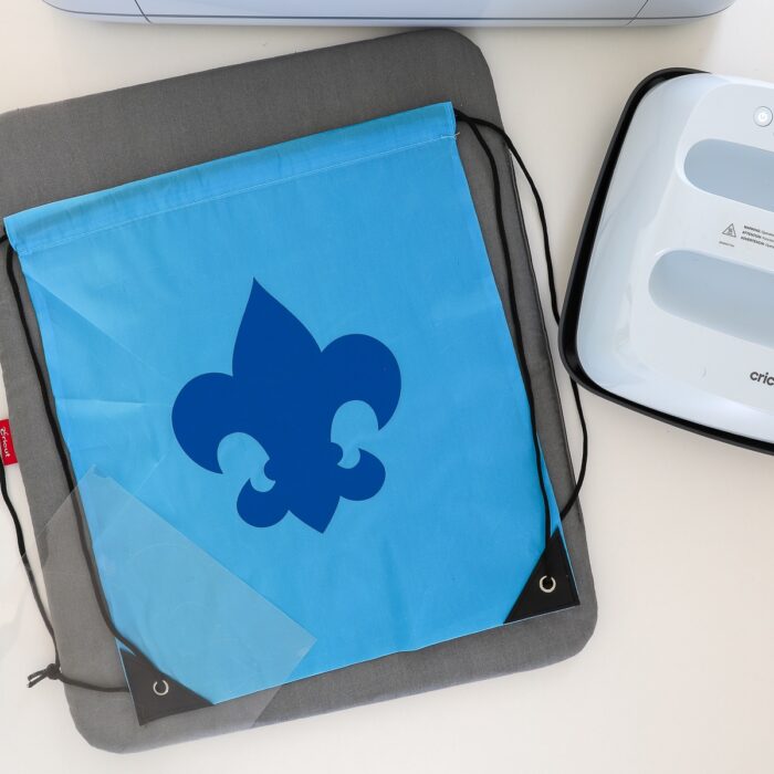 Lightblue drawstring backpack shown with iron-on decal next to Cricut EasyPress 3