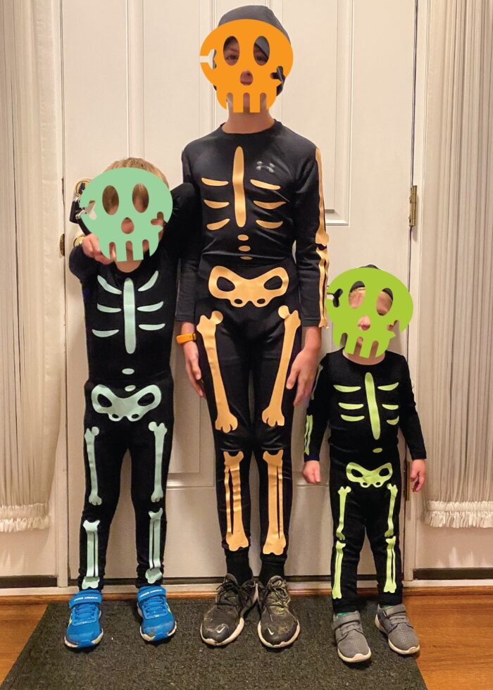 Three kids wearing homemade skeleton costumes in different colors