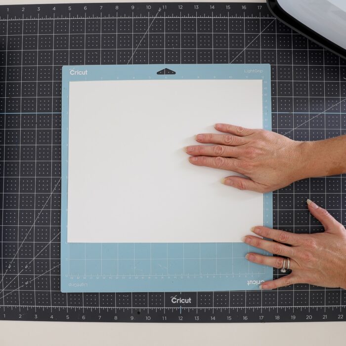 Hands placing glow-in-the-dark iron-on vinyl onto a light blue Cricut cutting mat