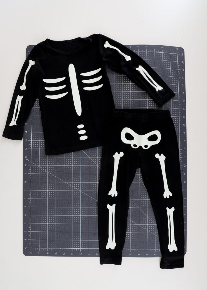Easy DIY skeleton costume made from iron-on vinyl and a black sweatsuit on top of a Cricut cutting mat