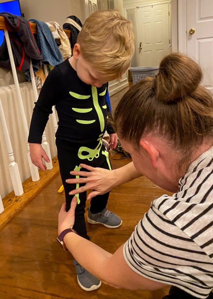 Toddler wearing black pajamas and Mom placing skeleton bone stickers onto him