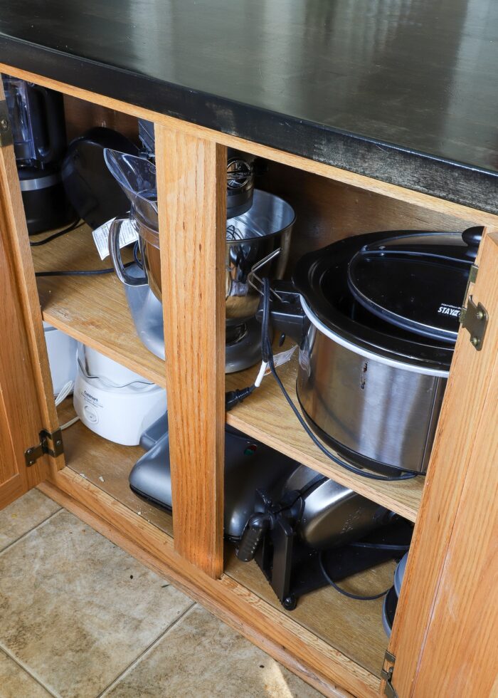 A mess of small kitchen appliances on lower cabinet shelves