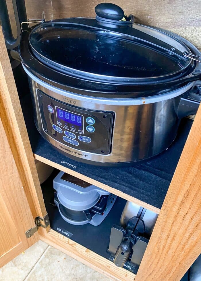 A crockpot and other small appliances organized inside a lower kitchen cabinet