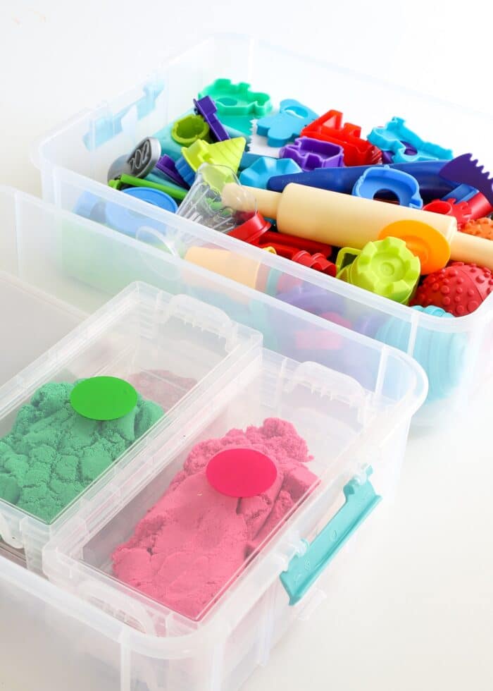 Two tiers of a stackable storage bin holding Kinetic sand and sand-related toys