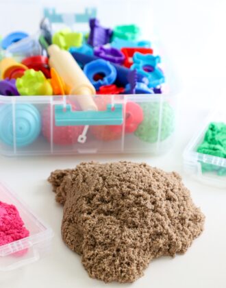 A pile of brown Kinetic Sand shown alongside a carrying caddy full of toys and tools