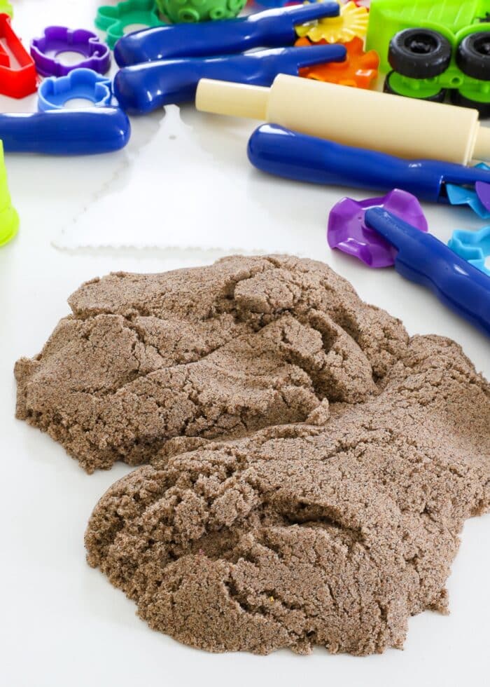 A pile of Kinetic sand on a white table shown alongside various toys and tools