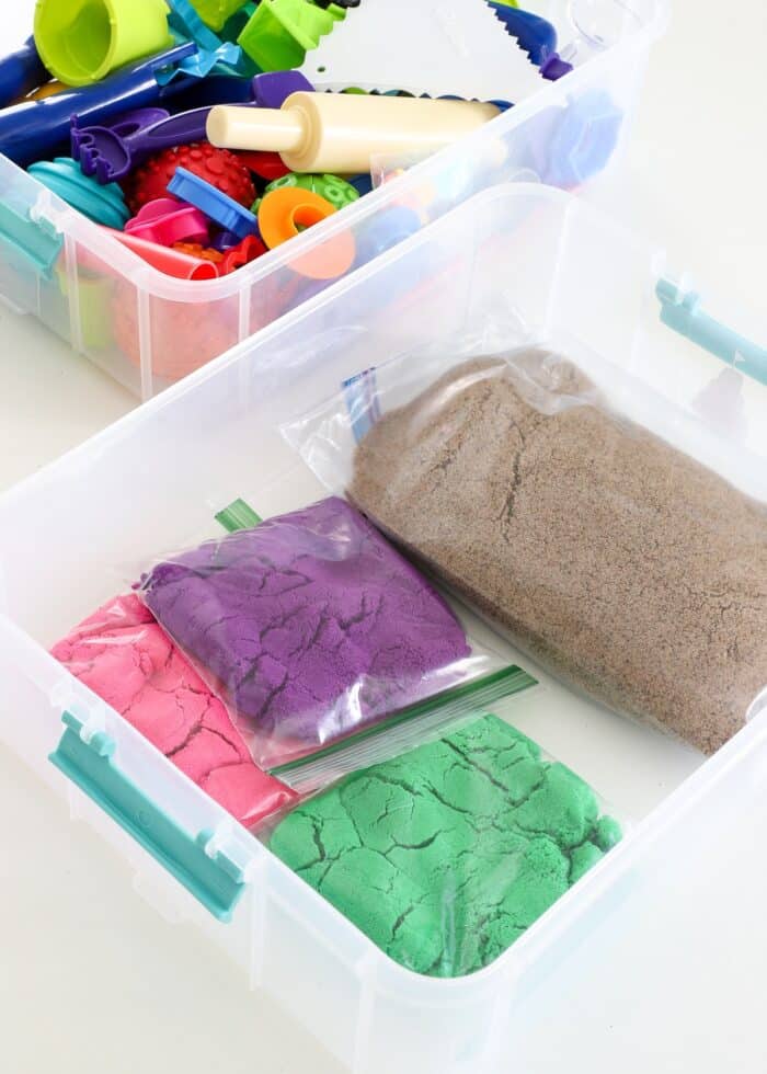 Plastic bags of Kinetic Sand loaded into the bottom of a plastic carrying caddy