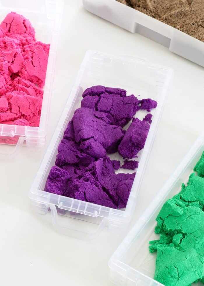 Pink, purple, and green Kinetic Sand loaded into clear plastic pencil boxes