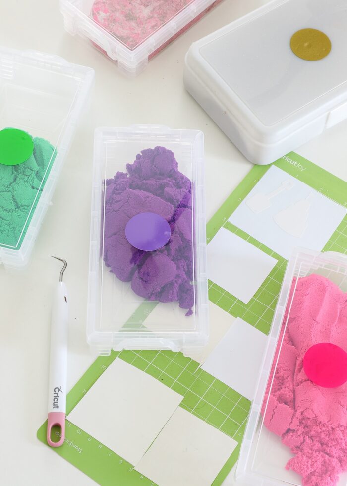 Colored stickers on the top of plastic boxes holding different colors of kinetic sand