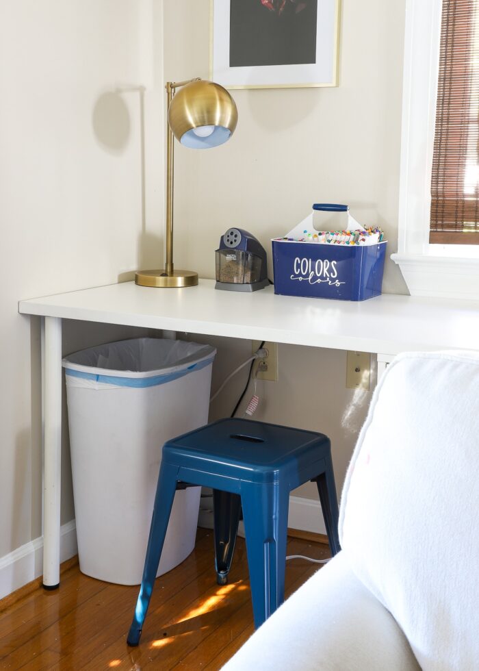 While desk with blue stool, gold lamp, and coloring caddy
