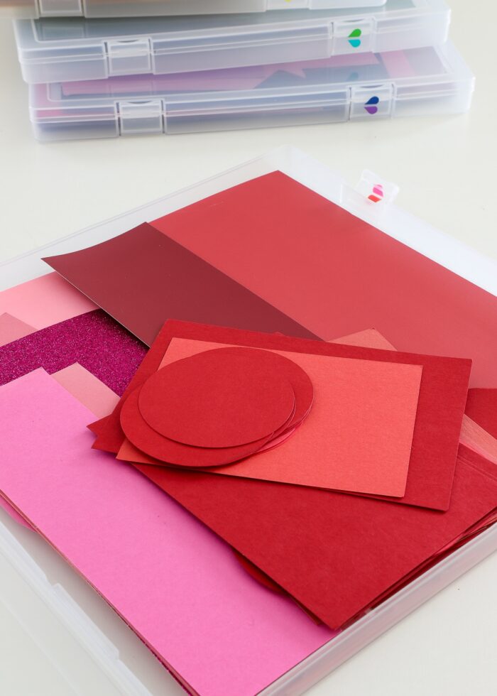 Red and pink paper scraps inside a clear craft paper storage box