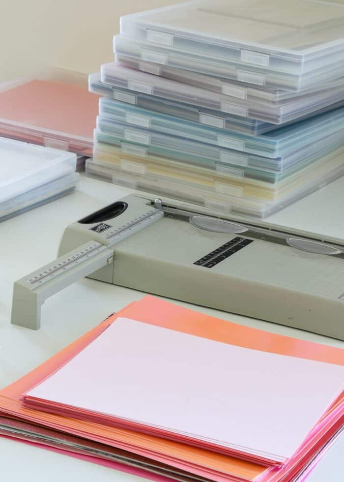 Paper trimmer shown alongside a stack of cardstock and clear plastic storage boxes