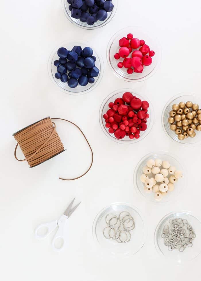 Red, white, blue, and gold wood beads shown with keychain hardware and leather cord on a white table