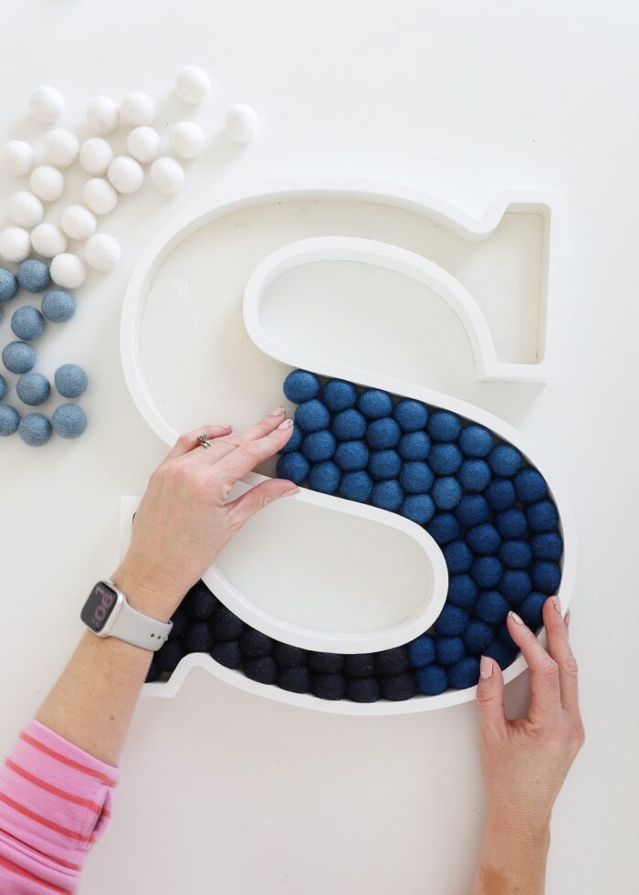 Process shot of loading blue felt balls into a wooden letter "S" tray
