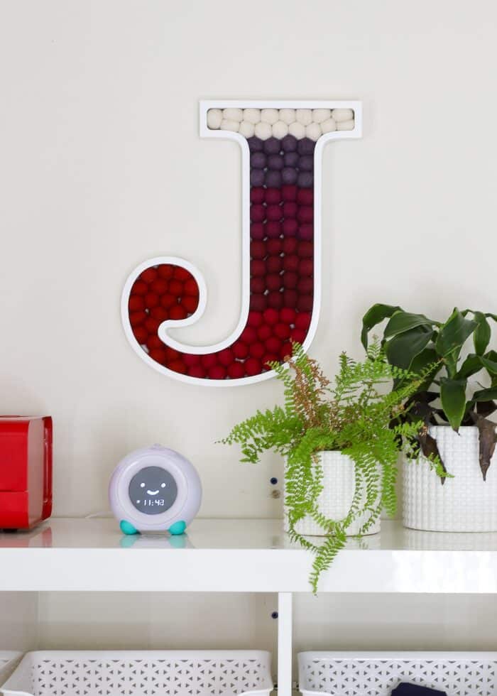 Pom Pom Letter J made with red and white felt balls hung on a wall