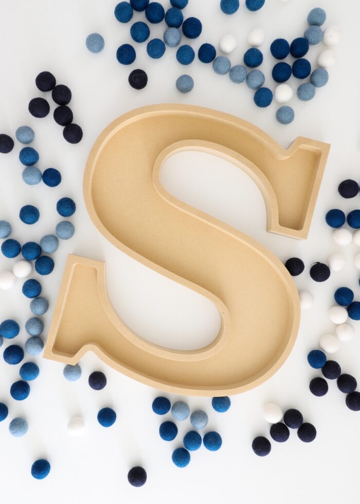 Unfinished letter tray "S" shown with blue and white felt balls