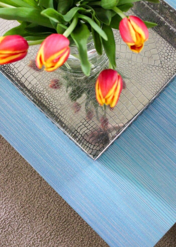 Top of coffee table covered in turquoise grasscloth wallpaper shown with tray and tulips