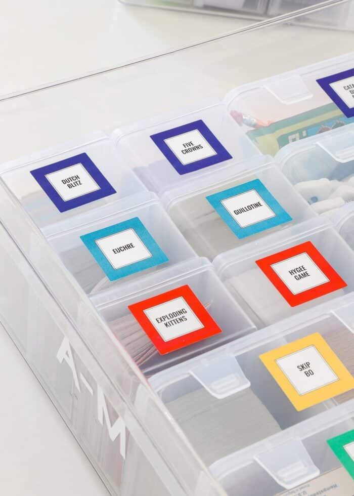Playing card games organized into clear plastic boxes, labeled with bright squares, and loaded into a large bin alphabetically