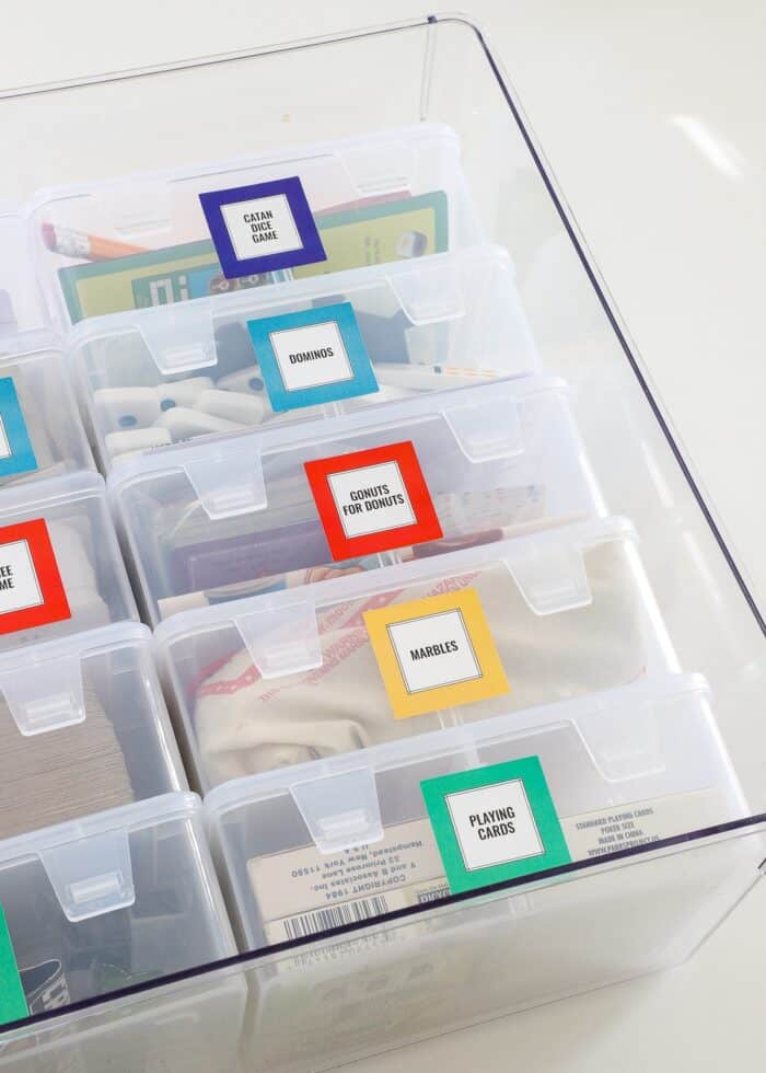 Playing card games organized into clear plastic boxes, labeled with bright squares, and loaded into a large bin alphabetically