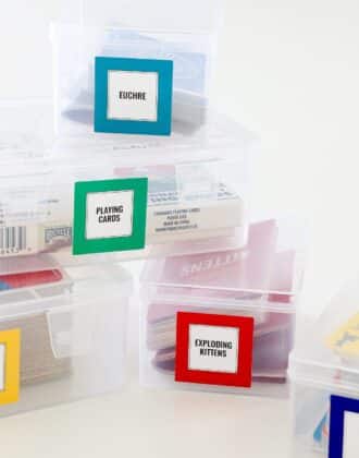 A stack of clear playing card storage boxes with brightly colored labels