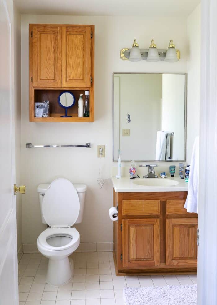 Builder-grade basic rental bathroom with oak cabinets and off white wall and tiles