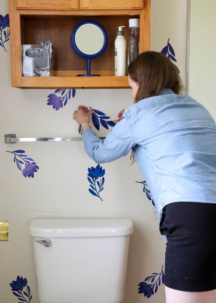 Megan placing blue flower wall decal on bathroom wall