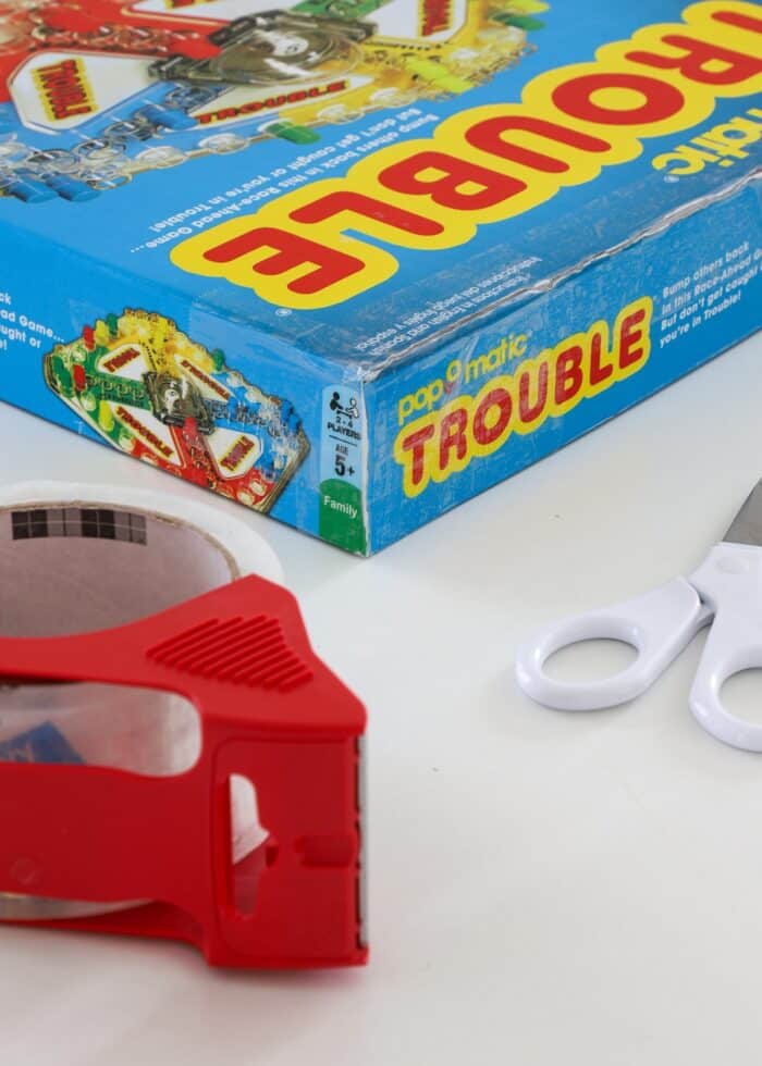 Repairing a broken Trouble game box with clear packing tape