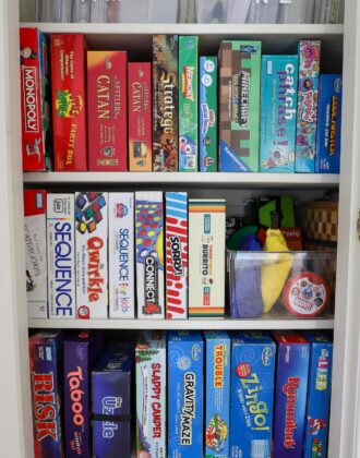 Three shelves of organized board games standing on their sides in rainbow color order