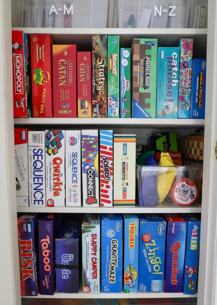 Three shelves of organized board games standing on their sides in rainbow color order