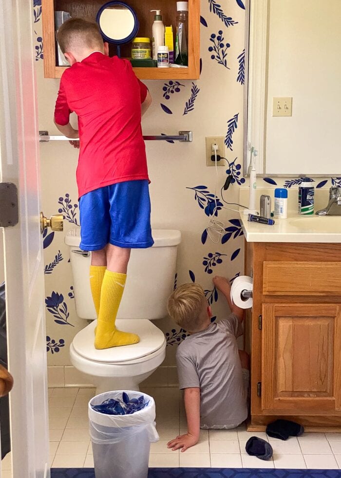 Two little boys peeling blue flower decals of a bathroom wall