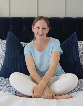 Megan in a blue shirt sitting on a white bedspread with blue pillows