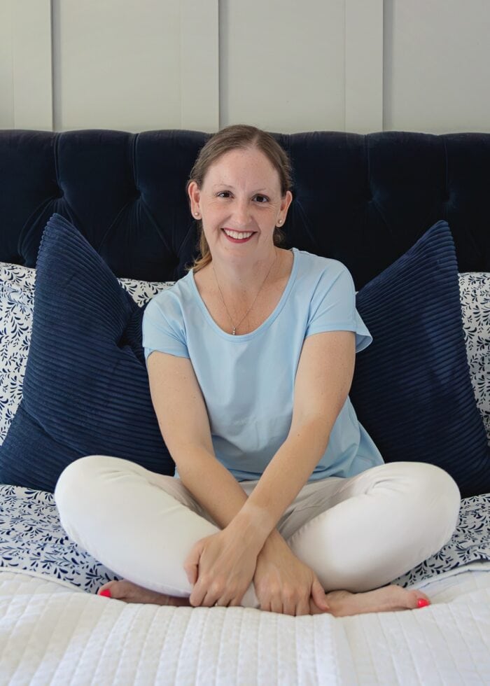 Megan in a blue shirt sitting on a white bedspread with blue pillows