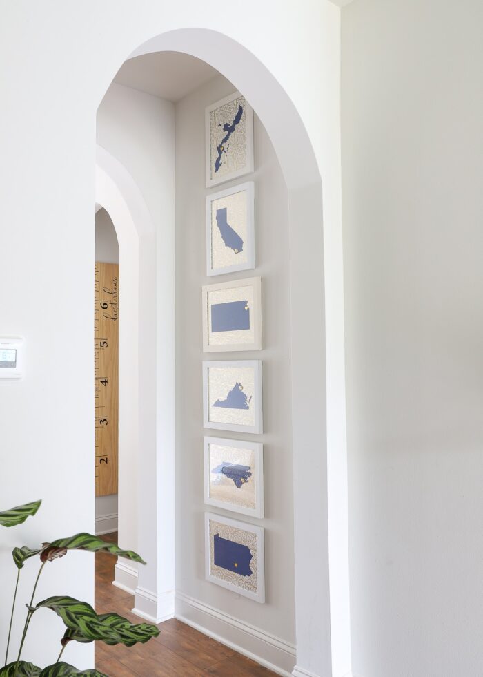 Blue, white, and gold State art prints on a white wall underneath an arched doorway