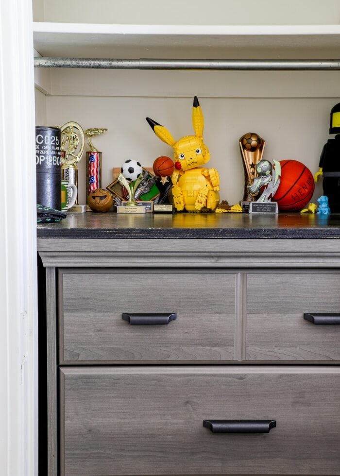 A grey dresser inside a closet topped with trophies and souvenirs