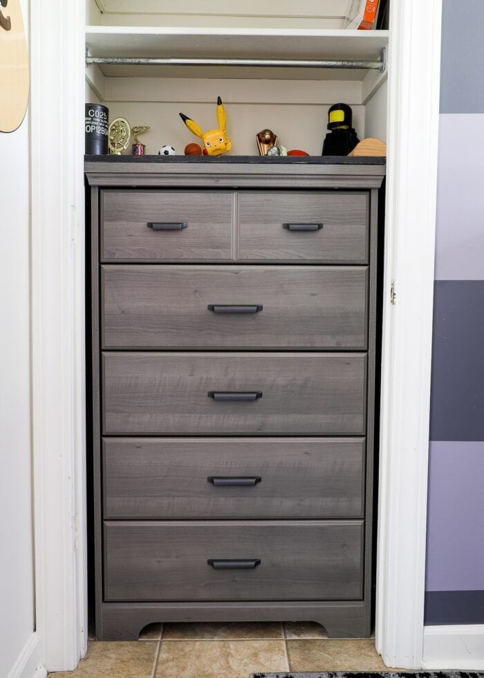 Tall grey dresser inside a skinny bedroom closet