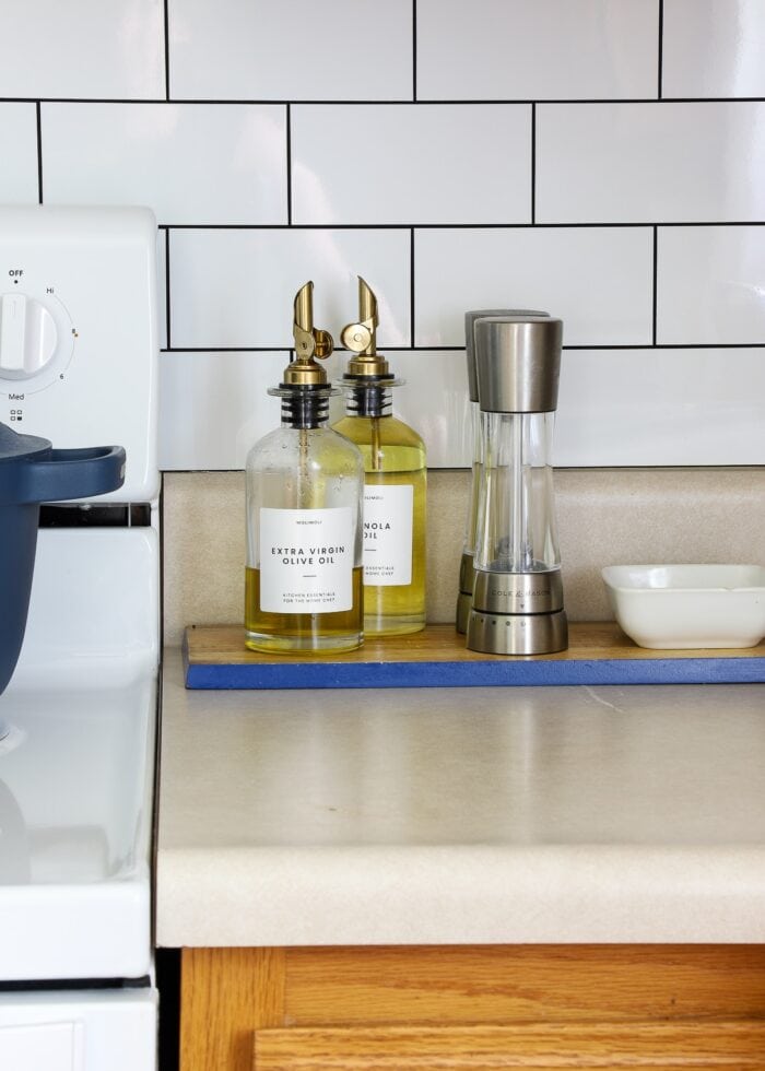 Oil dispensers and kitchen accessories shown on a wooden cutting board next to a kitchen stove