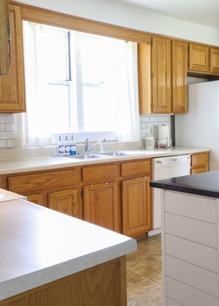 Plain white curtains hung on a tension rod above a rental kitchen window