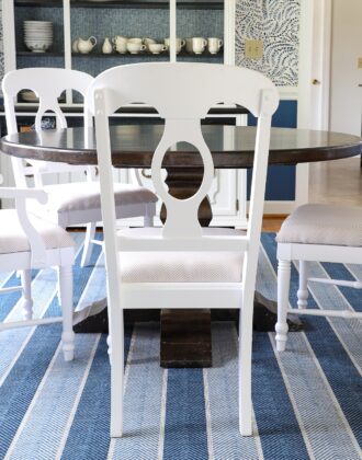 Blue striped rug under a wooden dining table and white chairs