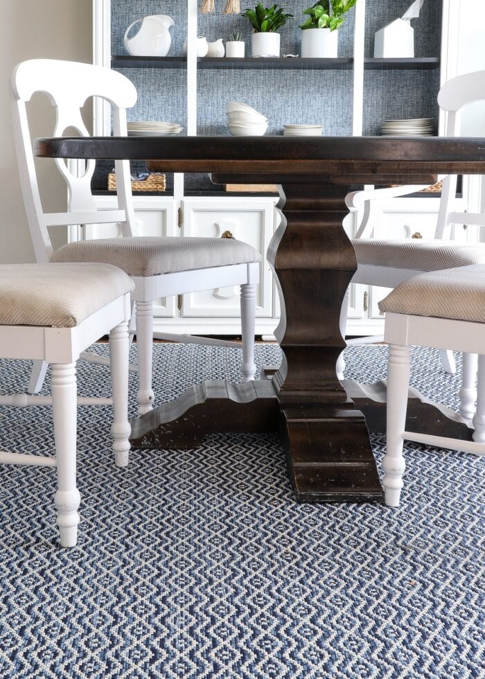 Blue and white diamond patterned outdoor rug under wooden dining room table with white chairs