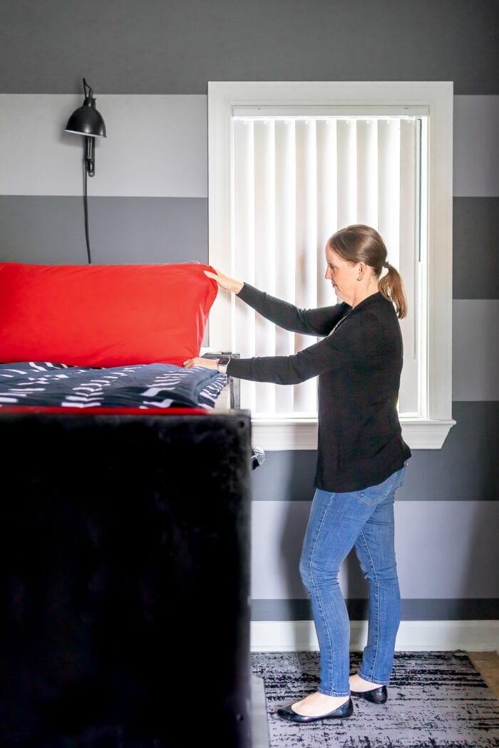 Megan fluffing a red pillow in a small grey, black, and red teen bedroom